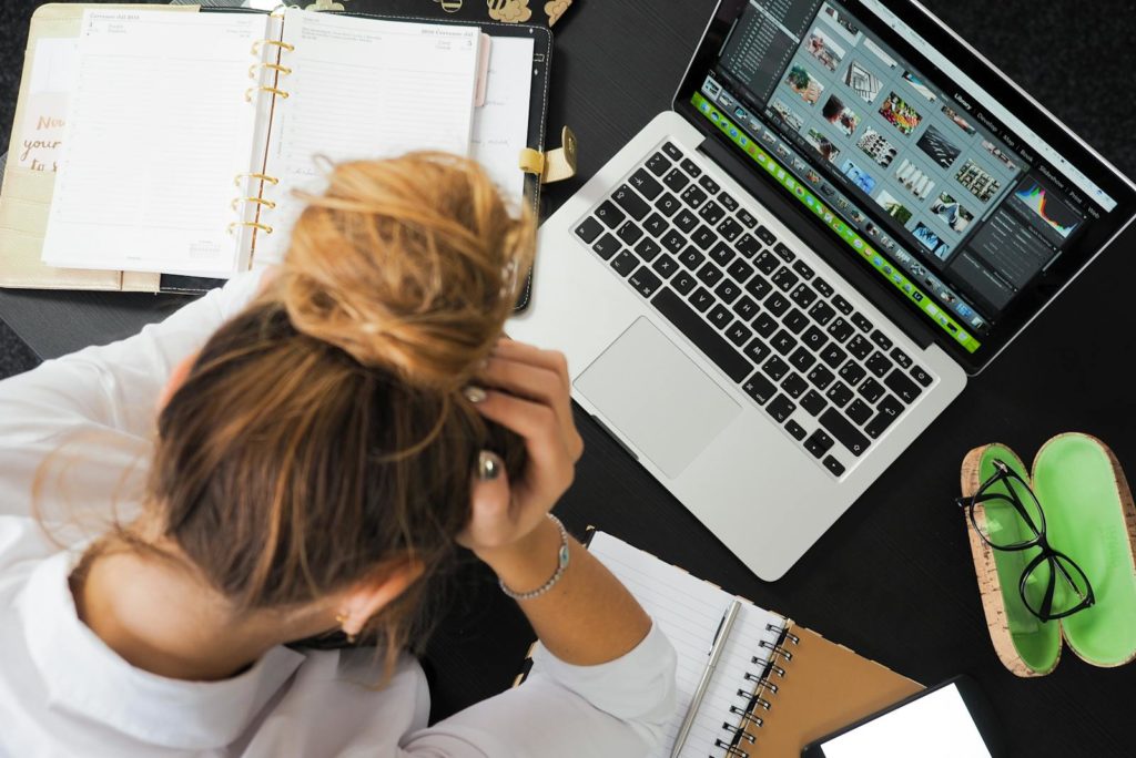 Vue aérienne d'une femme stressée travaillant à un bureau avec un ordinateur portable, un téléphone et des cahiers.