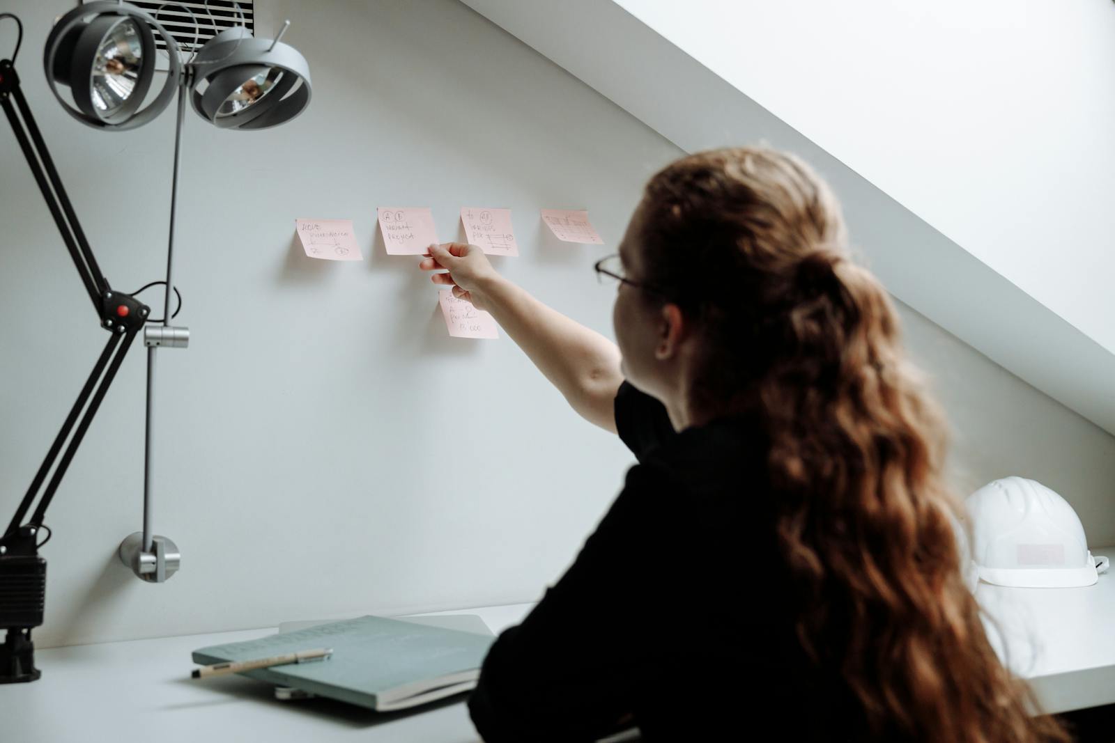 Une femme organise des notes autocollantes sur un mur dans un bureau élégant et moderne, favorisant ainsi la productivité et la concentration.